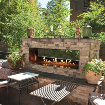 brick outdoor gas fireplace with patio furniture and greenery